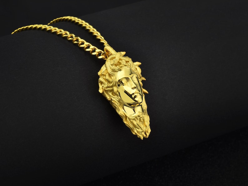 May include: A gold chain necklace with a pendant featuring a detailed, three-dimensional sculpture of a woman's face.