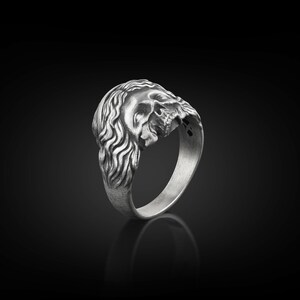 May include: A silver ring with a detailed skull design. The skull is depicted with a long, flowing mane of hair.