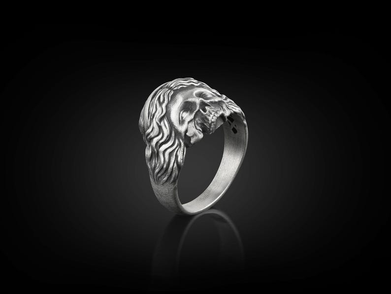 May include: A silver ring with a detailed skull design. The skull is depicted with a long, flowing mane of hair.