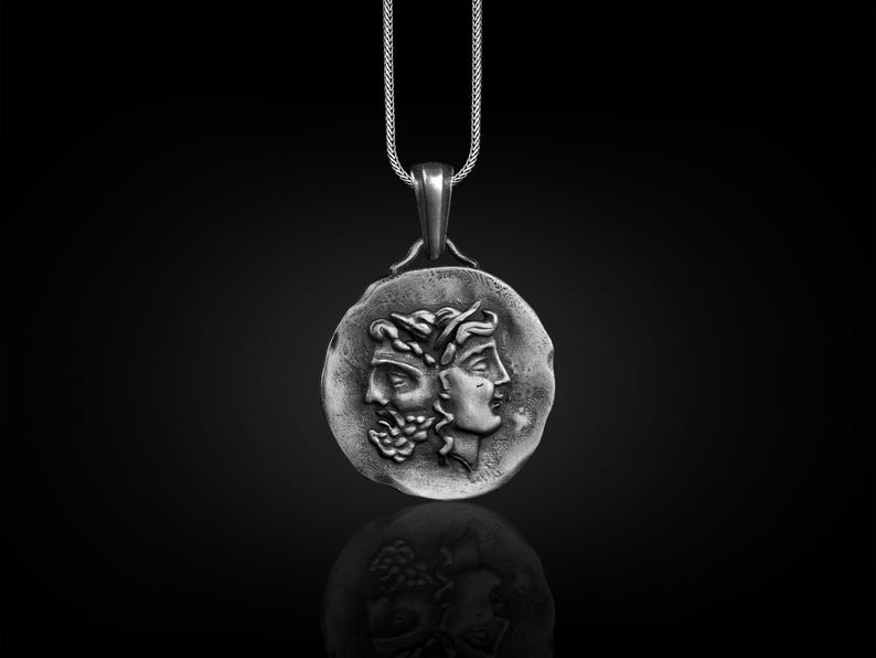 May include: A silver pendant necklace featuring a round coin with a detailed embossed design of two faces, one with a beard and the other with a crown.