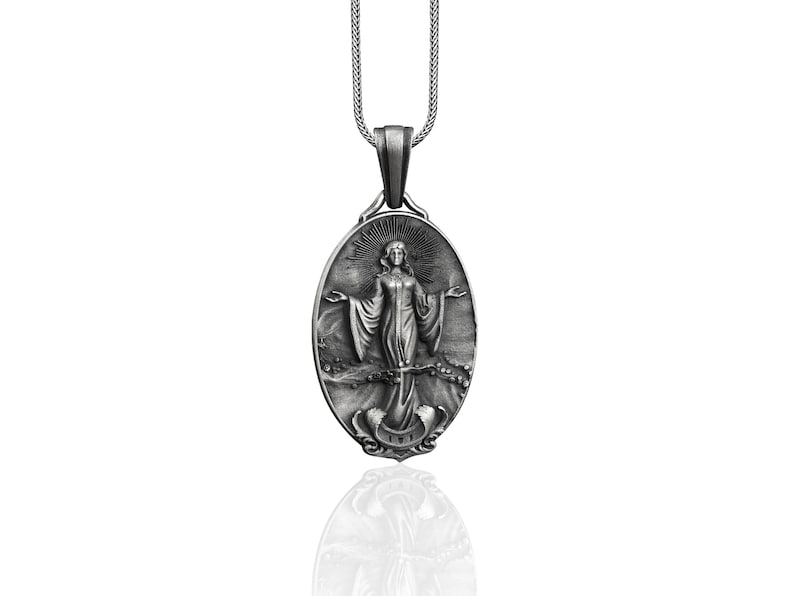 Puede incluir: Collar con colgante de plata con un dije ovalado detallado con una imagen en relieve de una mujer con los brazos extendidos. El dije tiene una superficie texturizada y un halo alrededor de la cabeza de la mujer.