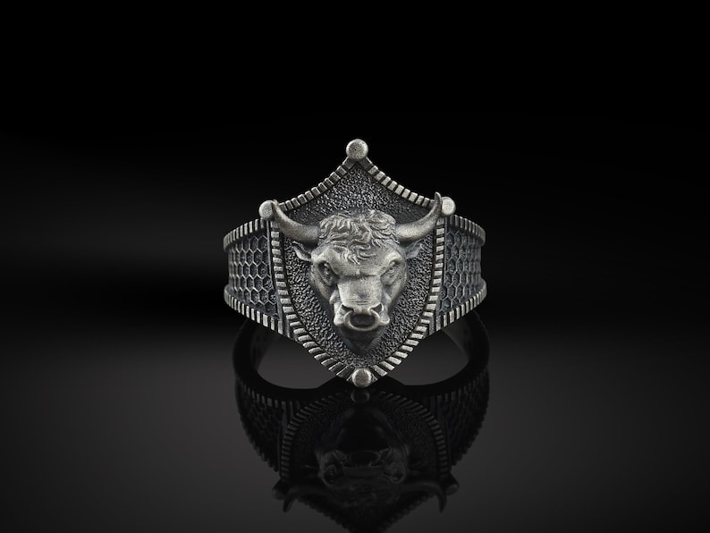 May include: A silver ring featuring a bull's head design on a shield-shaped setting. The ring has a textured band.