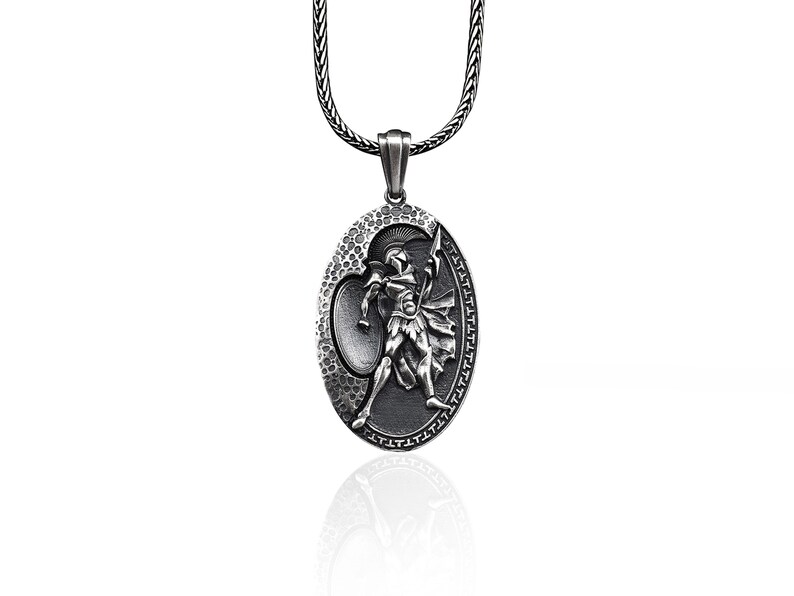 May include: Silver chain necklace with an oval pendant featuring a detailed relief of a warrior holding a spear and shield.