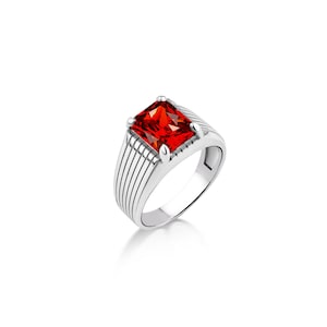 May include: A silver ring with a red square-shaped gemstone. The ring has a textured band with parallel lines.