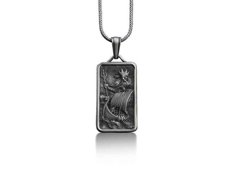 May include: A silver pendant necklace with a rectangular tag featuring a detailed engraving of a mythical sea god holding a trident and steering a ship.