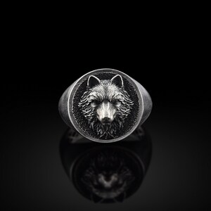May include: A silver ring featuring a wolf's head design. The wolf's head is raised and has a detailed fur texture.