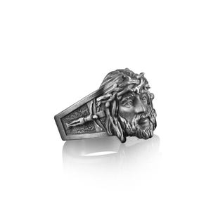 May include: A silver ring with a detailed depiction of Jesus' face with a crown of thorns. The ring band features a cross.