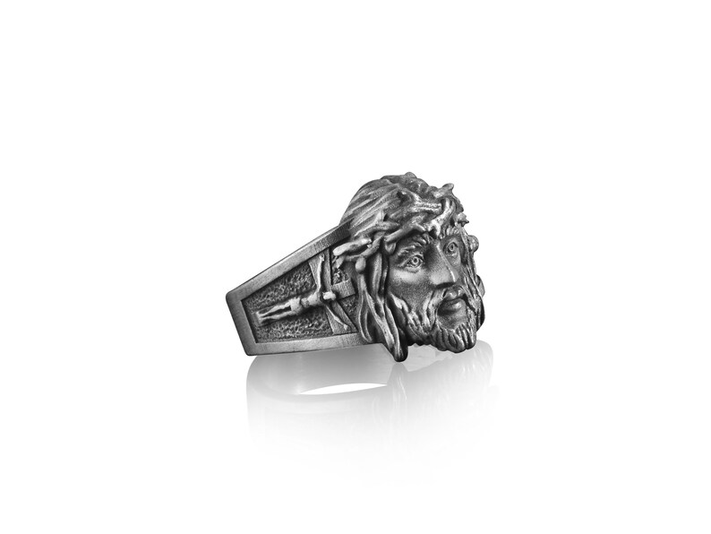 May include: A silver ring with a detailed depiction of Jesus' face with a crown of thorns. The ring band features a cross.