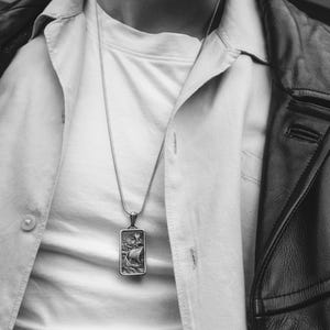 May include: A silver chain necklace with a rectangular pendant featuring a detailed engraving of a ship sailing on the water.