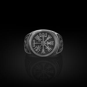May include: A silver ring with a detailed compass design featuring a circular pattern of symbols. The ring is on a black background.