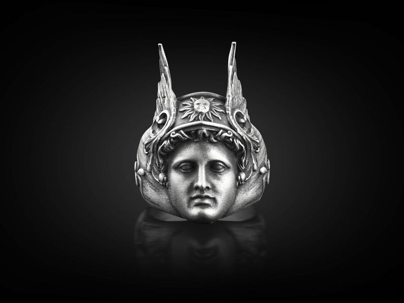 May include: A silver ring with a detailed design of a person's face wearing a winged helmet with a sun symbol on the front.