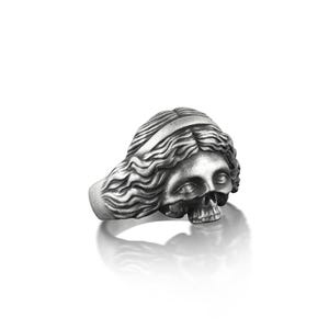 May include: A silver ring with a detailed skull design, the skull is depicted as a woman with long flowing hair.