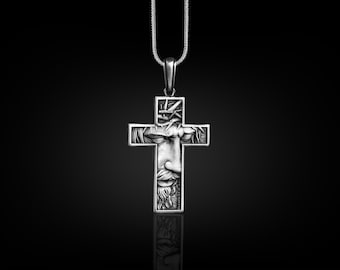 May include: A silver pendant necklace featuring a detailed cross with a depiction of Jesus' face within the cross.