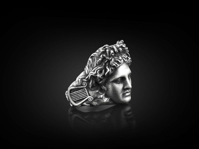 Peut inclure: Une bague en argent avec une sculpture d&eacute;taill&eacute;e d'une t&ecirc;te d'homme avec une lyre. La bague est de style classique.