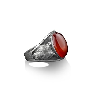 May include: A silver ring with a carved wolf head design and a red carnelian gemstone.