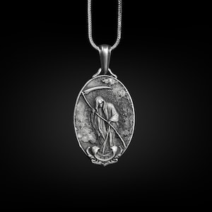 Puede incluir: Un collar con un colgante de plata que presenta una representaci&oacute;n detallada de la Muerte sosteniendo una guada&ntilde;a. El colgante tiene forma ovalada y una superficie texturizada.