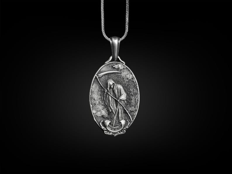 Puede incluir: Un collar con un colgante de plata que presenta una representaci&oacute;n detallada de la Muerte sosteniendo una guada&ntilde;a. El colgante tiene forma ovalada y una superficie texturizada.