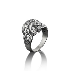 May include: A silver ring with a detailed skull design. The skull is depicted with a long, flowing mane of hair.