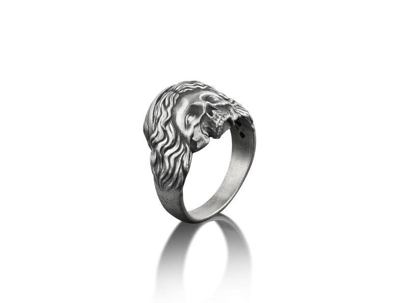 May include: A silver ring with a detailed skull design. The skull is depicted with a long, flowing mane of hair.