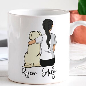 Op de afbeelding: Witte keramische mok met een cartoonillustratie van een vrouw met lang zwart haar en een witte hond. De tekst "Roscoe Emily" staat op de mok gedrukt.