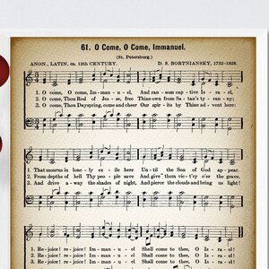 以下が含まれることがあります： 「O Come, O Come, Immanuel」というクリスマスキャロルのヴィンテージ楽譜プリント。楽譜は、茶色がかった色合いの古びた紙に印刷されています。楽譜は黒インクで印刷されています。キャロルのタイトルはページの上部に太字で印刷されています。歌詞は楽譜の下に印刷されています。楽譜は白いフレームで額装されています。