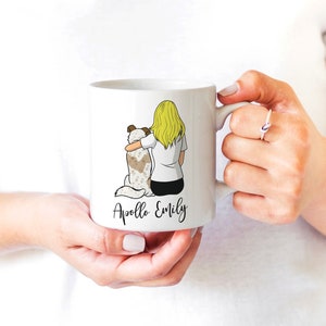 May include: White ceramic mug with a cartoon illustration of a woman with blonde hair hugging a dog. The text "Apollo Emily" is printed on the mug.