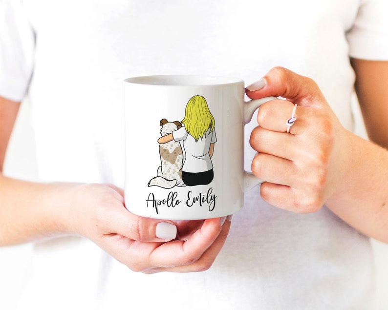 May include: White ceramic mug with a cartoon illustration of a woman with blonde hair hugging a dog. The text "Apollo Emily" is printed on the mug.