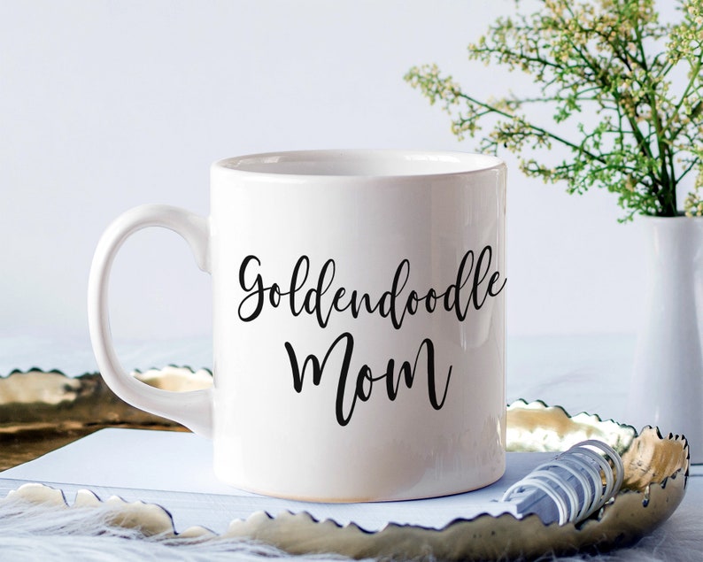 Op de afbeelding: Witte keramische koffiemok met zwarte tekst die "Goldendoodle Mom" luidt.