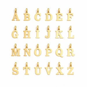 Puede incluir: Colgantes dorados con letras del alfabeto, de la A a la Z, sobre un fondo blanco. Cada colgante presenta una fuente serif clásica y un pequeño lazo para una cadena. Ideal para joyería personalizada.