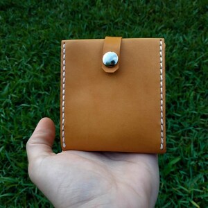 Peut inclure: Un petit portefeuille en cuir marron avec des d&eacute;tails de couture blanche et une fermeture &agrave; pression argent&eacute;e.