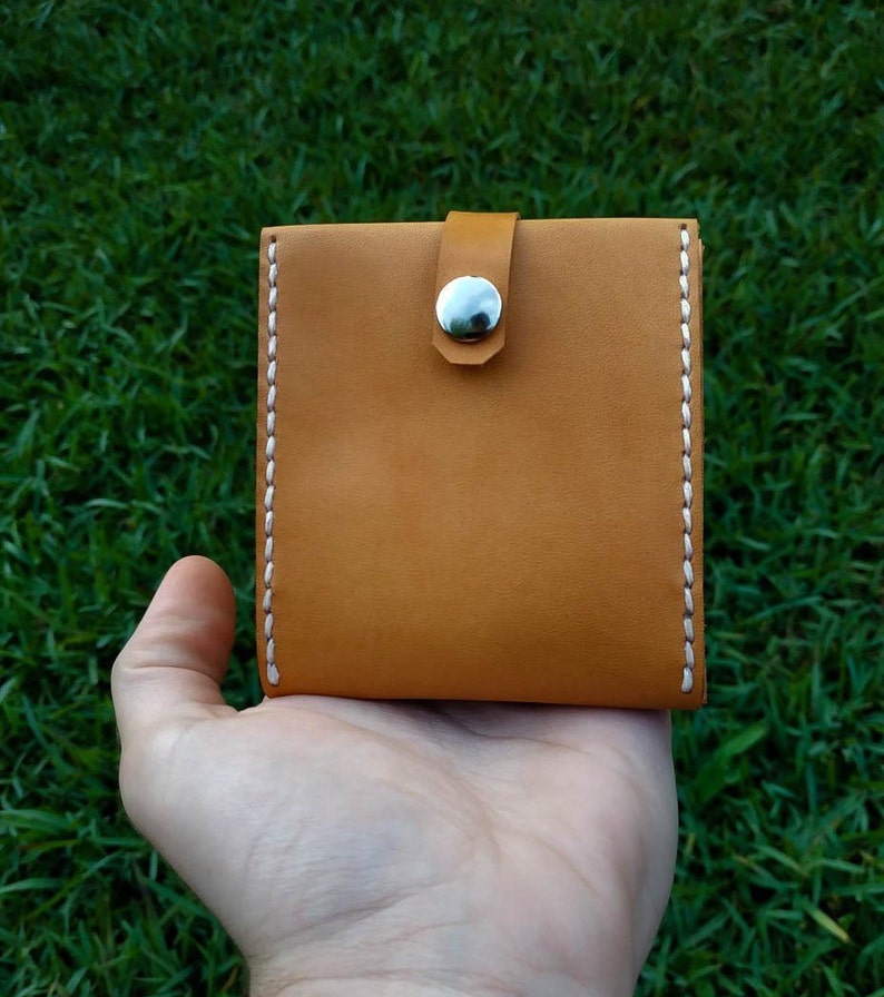 Peut inclure: Un petit portefeuille en cuir marron avec des d&eacute;tails de couture blanche et une fermeture &agrave; pression argent&eacute;e.