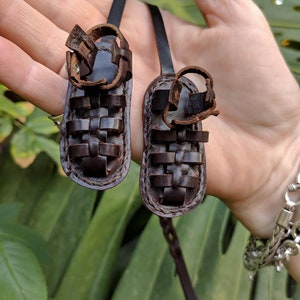 May include: A pair of brown leather sandals with a woven design. The sandals are attached to a brown leather cord.