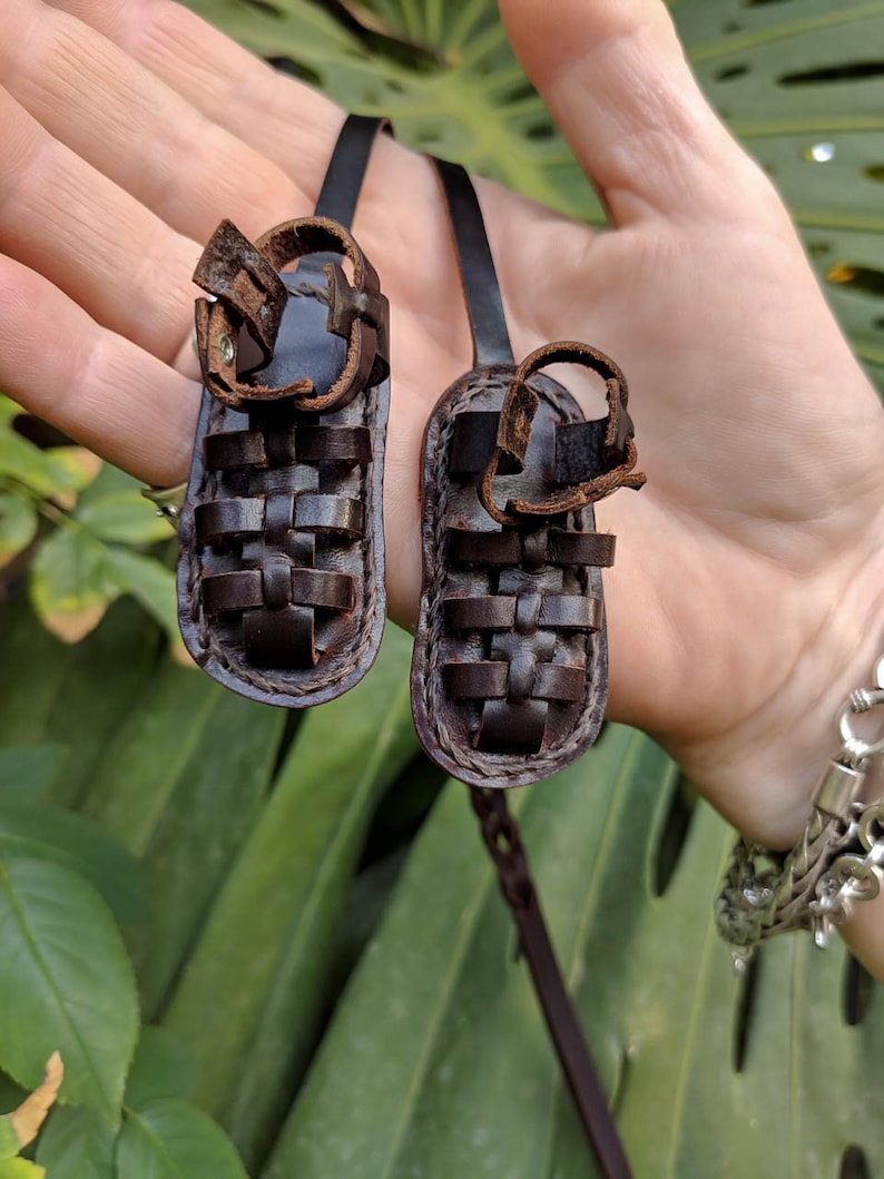 May include: A pair of brown leather sandals with a woven design. The sandals are attached to a brown leather cord.