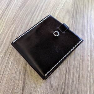Peut inclure: Un portefeuille en cuir marron fonc&eacute; avec des coutures blanches sur les bords. Le portefeuille a un petit rabat avec une fermeture &agrave; bouton.