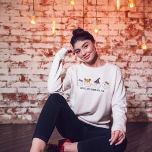 Puede incluir: Una sudadera blanca con un gr&aacute;fico de cuatro fantasmas con disfraces de Halloween. El texto en la sudadera dice "Ghosts just wanna have fun."