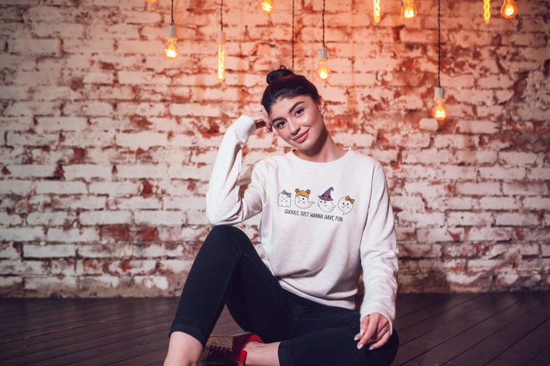 Puede incluir: Una sudadera blanca con un gr&aacute;fico de cuatro fantasmas con disfraces de Halloween. El texto en la sudadera dice "Ghosts just wanna have fun."