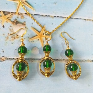 May include: A gold chain necklace with a green glass pendant and matching earrings. The pendant and earrings feature a gold circle with a green glass bead in the center.