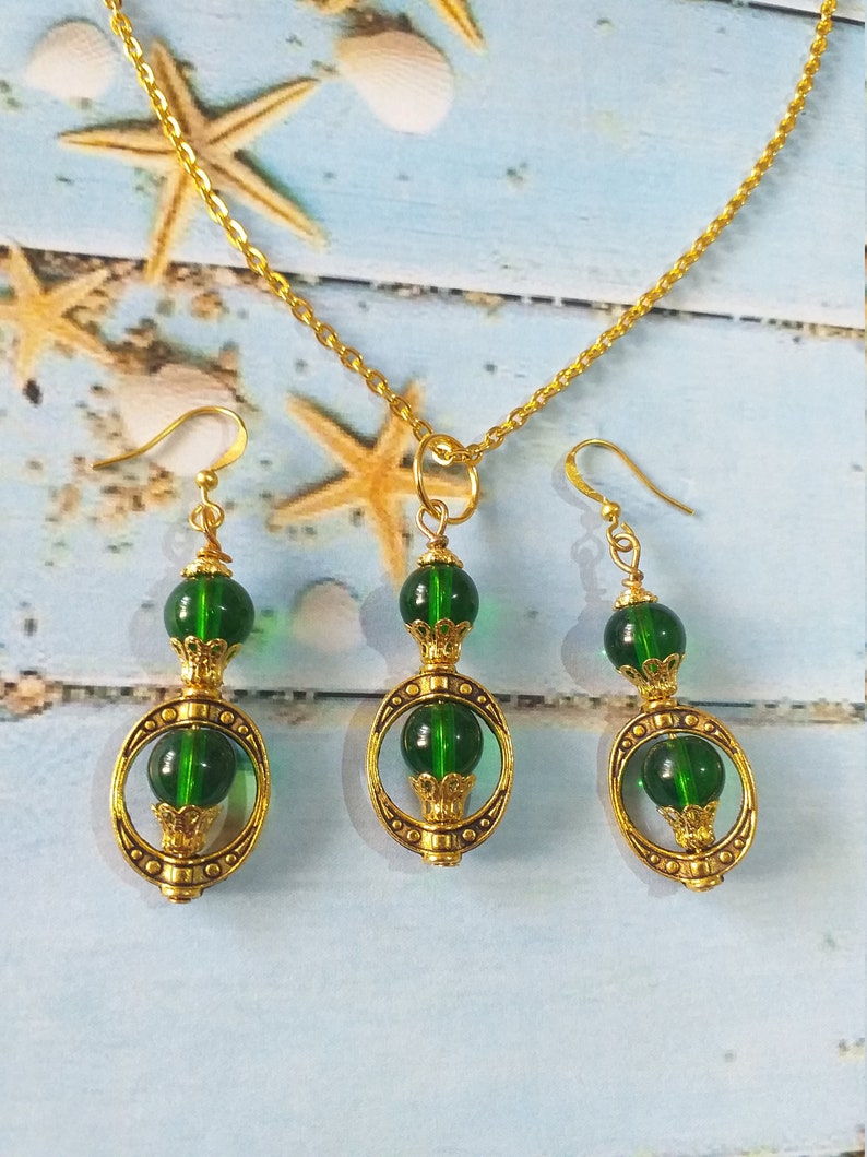 May include: A gold chain necklace with a green glass pendant and matching earrings. The pendant and earrings feature a gold circle with a green glass bead in the center.