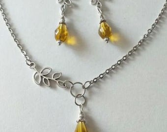 May include: A silver chain necklace with a small leaf charm and a teardrop-shaped amber crystal pendant. Matching earrings with leaf charms and amber crystal drops.