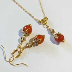 K&ouml;nnte beinhalten: Ein goldenes Halsketten- und Ohrring-Set mit orangefarbenen Edelsteinperlen und verzierten goldenen Akzenten.