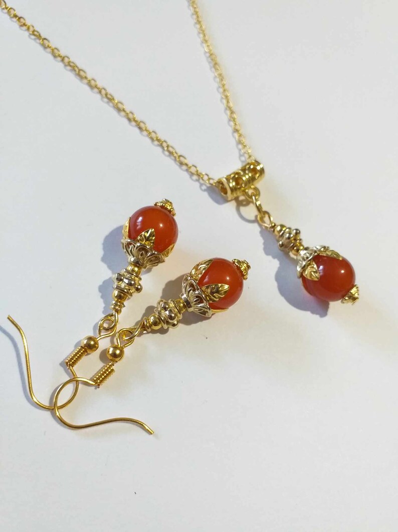 K&ouml;nnte beinhalten: Ein goldenes Halsketten- und Ohrring-Set mit orangefarbenen Edelsteinperlen und verzierten goldenen Akzenten.