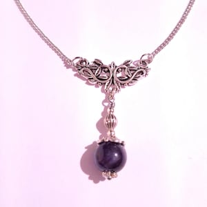 Puede incluir: Un collar de cadena de plata con un colgante de plata con un dise&ntilde;o floral y una piedra preciosa de color p&uacute;rpura oscuro.