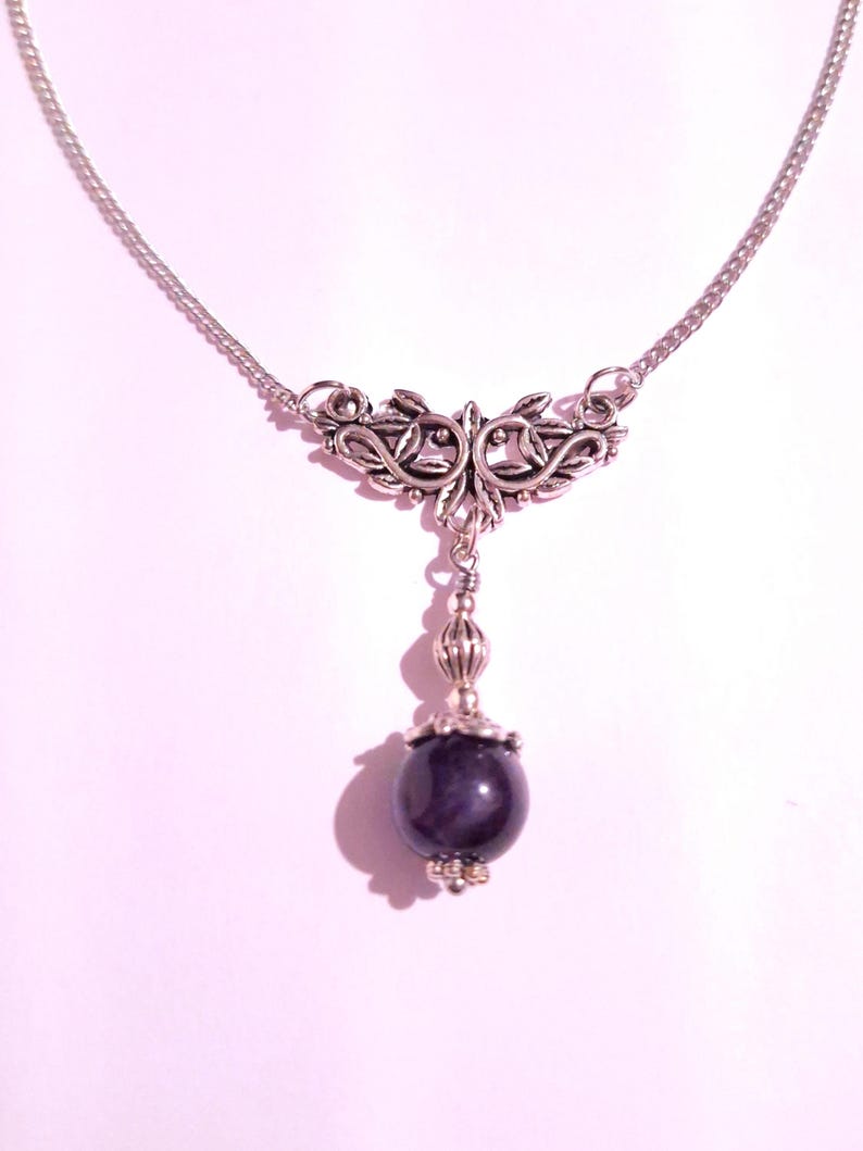 Puede incluir: Un collar de cadena de plata con un colgante de plata con un dise&ntilde;o floral y una piedra preciosa de color p&uacute;rpura oscuro.