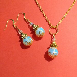May include: A gold necklace and earrings set with a light blue opal pendant and matching earrings. The pendant and earrings have a gold filigree design.