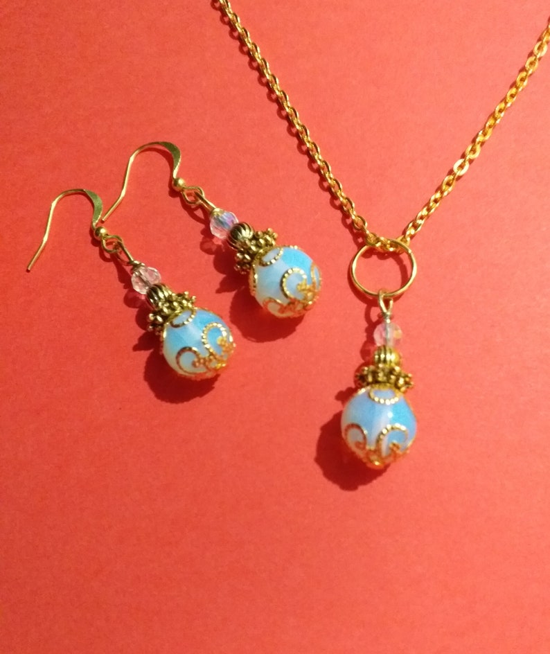 May include: A gold necklace and earrings set with a light blue opal pendant and matching earrings. The pendant and earrings have a gold filigree design.