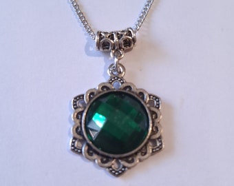 Puede incluir: Un collar de cadena de plata con un colgante de piedra preciosa verde. El colgante está rodeado por un diseño de filigrana de plata.