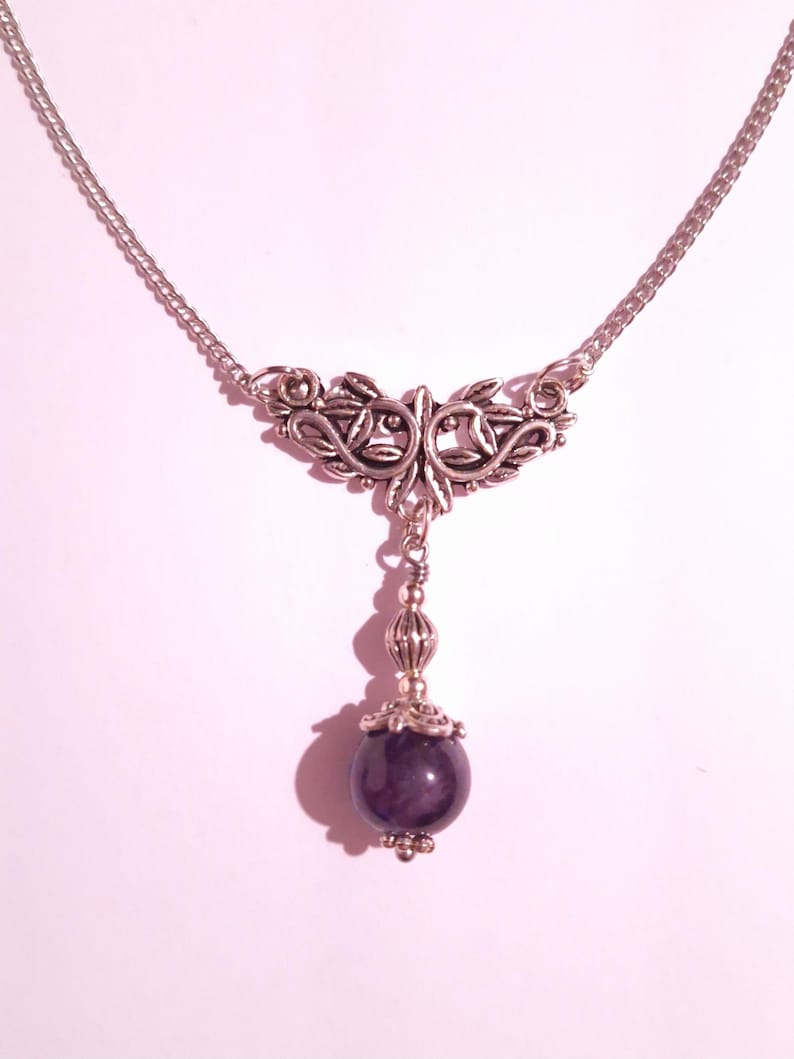 May include: A silver chain necklace with a silver pendant featuring a floral design and a dark purple gemstone.