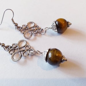 May include: A pair of silver earrings with a knot design and a brown tiger's eye stone dangle.