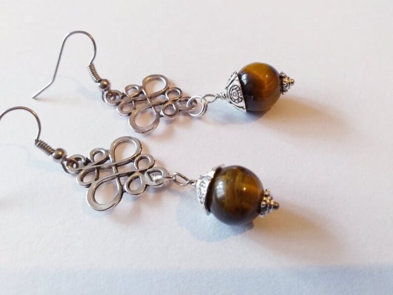 May include: A pair of silver earrings with a knot design and a brown tiger's eye stone dangle.