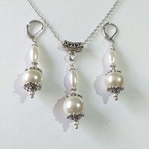 May include: A silver necklace and earrings set with white pearl beads and ornate silver accents.